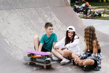 Kids smile and laugh and have fun together. Children with skateboard and penny boards communicate and discuss on the sports playground. Boy and girls friendship concept
