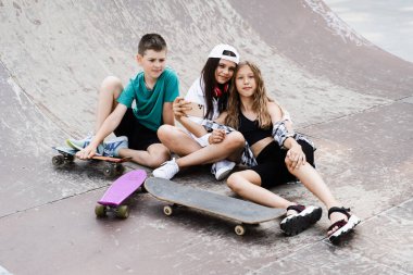 Children with skateboard and penny boards making selfie on phone on the sports playground. Children friendship concept. Kids smile and laugh and have fun together