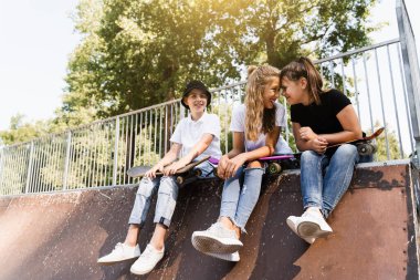 Children with skateboard and penny boards communicate and discuss on the sports playground. Children friendship concept. Children smile and laugh and have fun together