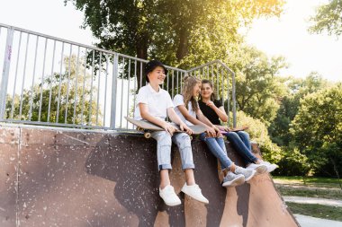 Kids smile and laugh and have fun together. Children with skateboard and penny boards communicate and discuss on the sports playground. Boy and girls friendship concept