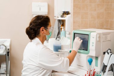 Laboratuvar asistanı kan analizi üzerinde çalışıyor ve laboratuvarda hematolojik analiz yapıyor. Laboratuvarda tıbbi malzemeler var. Kanın biyokimyasal ve hematolojik analizi