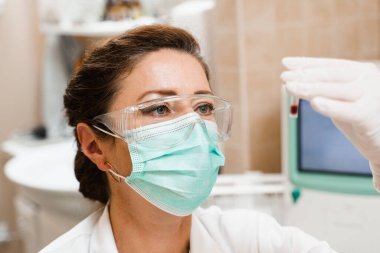 Laboratuvar asistanı elinde kanla test tüpünü tutuyor ve bakıyor. Laboratuvarda kan testi. Gözlüklü ve maskeli tıp bilimcisi