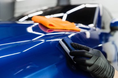 Otomobil servisinde sünger kullanılarak seramik koruyucu kaplama uygulanması. Araba servisi çalışanı arabayı çiziklerden korumak için seramik kaplama uygular.