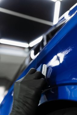 Otomobil servisinde sünger kullanılarak seramik koruyucu kaplama uygulanması. Araba servisi çalışanı arabayı çiziklerden korumak için seramik kaplama uygular.