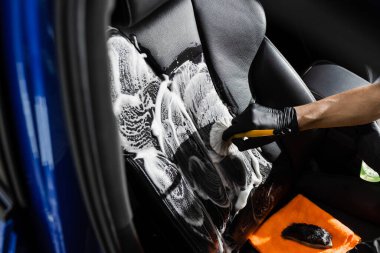 Fırça kullanarak köpük ve deterjan temizleme koltuğu. Otomotiv temizleme servisinde çalışan bir işçi. Araç iç dekorasyonu