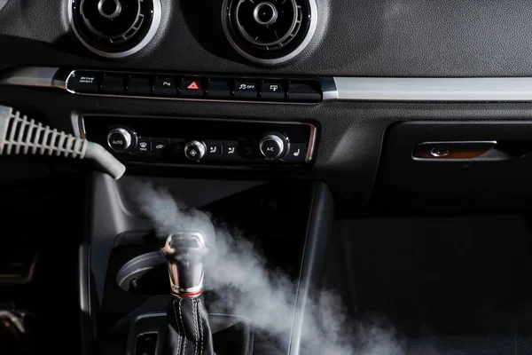 Steam cleaning of gearbox and dashboard in car. Vaping steam. Cleaning individual elements of black leather interior in auto. Creative advert for auto detailing service