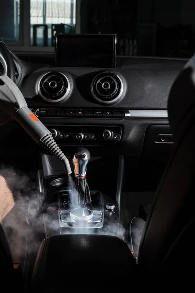 Steam cleaning of gearbox and dashboard in car. Vaping steam. Cleaning individual elements of black leather interior in auto. Creative advert for auto detailing service