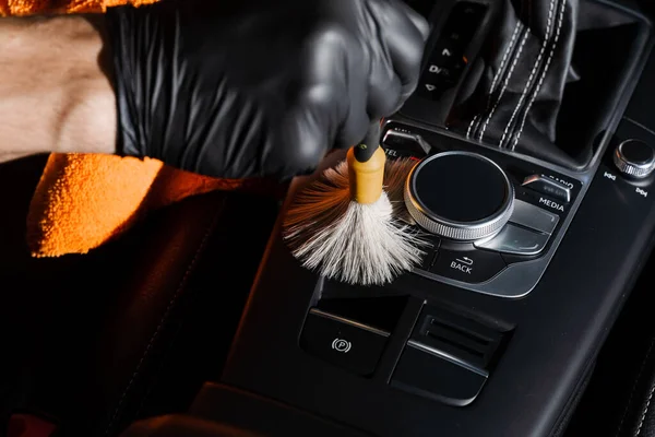 Dry cleaning with brush of gearbox and dashboard in car. Auto detailing service. Cleaning individual elements of black leather interior in auto
