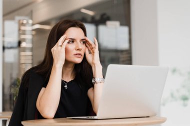Güçlü baş ağrısı olan kadın yönetici bilgisayarla beyaz ofiste çalışıyor. Dizüstü bilgisayarı olan üzgün bir kızın ağrıdan migreni tuttu.