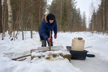 Bir adam kışın plastik fıçıdaki bir kaynaktan su çeker.