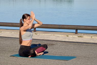 Genç bir kadın sabahın erken saatlerinde iskelede ısınıyor, nehrin arka planına karşı.