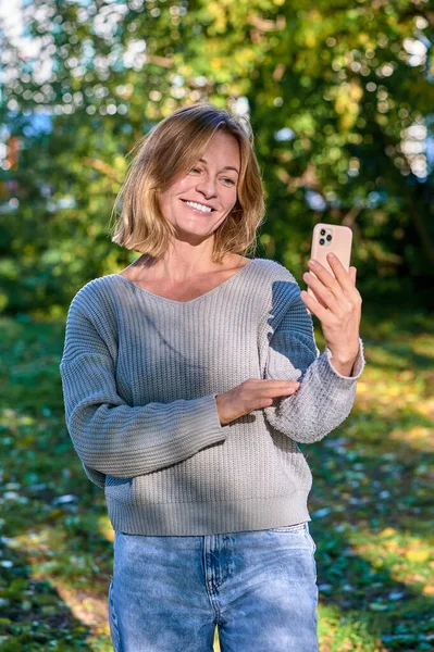 En kvinna i en park på sommaren talar under ett videosamtal på telefon — Stockfoto