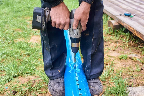 Açık havada tornavidayla plastik mavi boruda delik açmak.