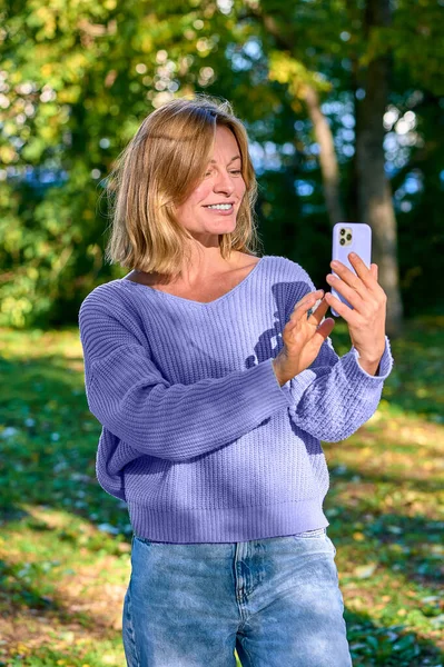 En kvinna i en park på sommaren talar under ett videosamtal på telefon — Stockfoto
