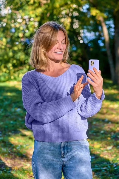 En kvinna i en park på sommaren talar under ett videosamtal på telefon — Stockfoto