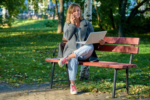 Женщина с ноутбуком сидит на скамейке в парке в солнечный летний день — стоковое фото