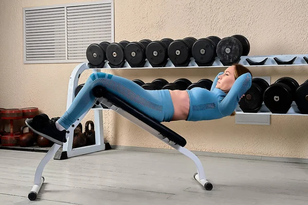 Güzel genç bir kadın spor salonundaki bir bankta karın kaslarını sallıyor.