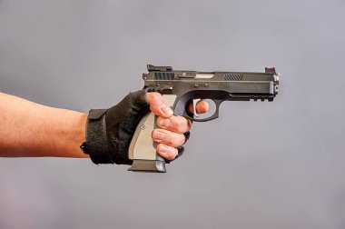 Adamın biri elinde gri bir arka planda siyah bir tabanca tutuyor.