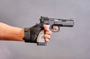 Adamın biri elinde gri bir arka planda siyah bir tabanca tutuyor.