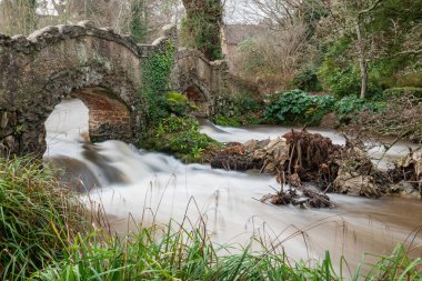 Lond exposure of the river Avill flowing under Lovers bridge in the grounds of Dunster castle in Somerset