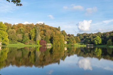 Wiltshire 'daki Stourhead bahçesindeki gölün etrafındaki sonbahar renklerinin görüntüsü