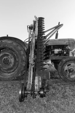 Antika bir çim biçme makinesi eski bir traktöre monte edilmiş.