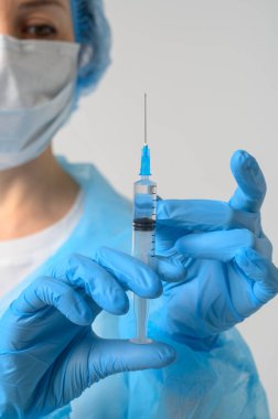 Tıbbi maskeli ve lastik eldivenli bir hemşire aşılı bir şırınga tutuyor.