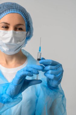 Tıbbi maskeli ve lastik eldivenli bir hemşire aşılı bir şırınga tutuyor.