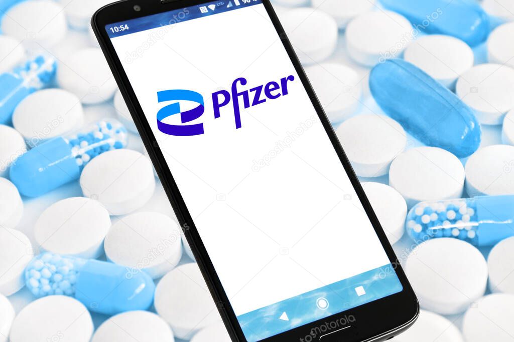 Hamburg, Germany - November 17  2021: Smartphone with Pfizer Logo against blue tablets and capsules Background