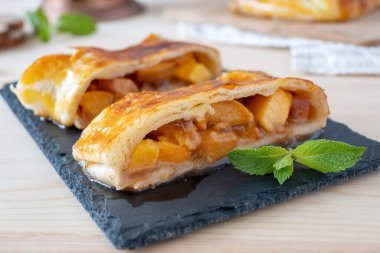 Kahverengi Şeftalili Strudel kahvaltıda mutfakta servis tahtasında. Nane yaprağıyla süslenmiş güney meyveli Sulu Turta dilimleri..