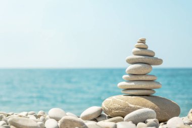 Güneşli bir günde deniz sahilinde dengeli çakıl taşı yığını. Sahildeki taş piramitlerle doğal yaz uyumu kavramı.