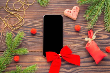 Ahşap arka planda Noel hediyesi olarak kırmızı yay ve boş siyah ekran ile akıllı telefon, üst görünüm