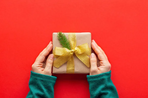 Vrouwelijke Handen Turquoise Trui Met Kerstcadeau Papieren Omslag Rode Achtergrond — Stockfoto