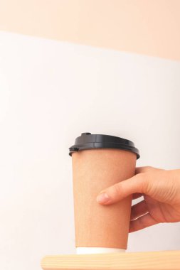 Elleri tek kullanımlık kahve bardağını ahşap masaya, ön tarafa, fotokopi odasına koymak için tutuyor. Kadınların elinde, masanın kenarındaki kahve paketleri..