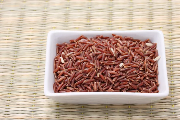 Arroz de jazmín rojo en tazón cuadrado blanco sobre estera de caña —  Fotos de Stock