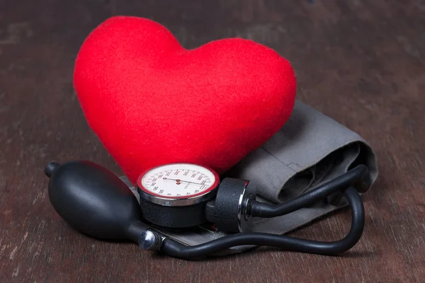 Medico, misura la pressione sanguigna con cuore rosso sul tavolo di legno — Foto Stock