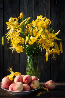 오래 된 나무 바탕에 복숭아와 유리 꽃병에 백합