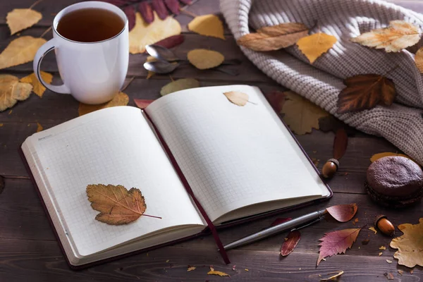 Sonbahar sezonu konsepti, güzel sonbahar kompozisyonu defter, çay, sonbahar yaprakları, kırsal ahşap masa üzerinde çikolatalı badem kurabiyesi.