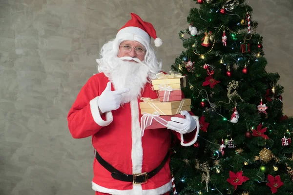 Fat Caucasian old mature man in costume Santa Claus happy white beard smiling holding gift boxes preparing decorations for Christmas tree festival celebration. Merry Christmas happy new year concept