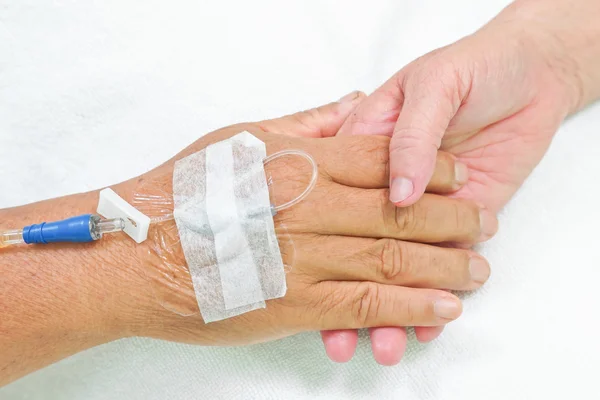 Mãos velhas segurando um ao outro com solução IV na mão de um paciente — Fotografia de Stock