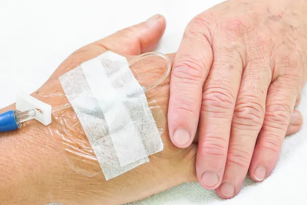 Manos viejas agarrándose unas a otras con solución intravenosa en la mano de un paciente — Foto de Stock