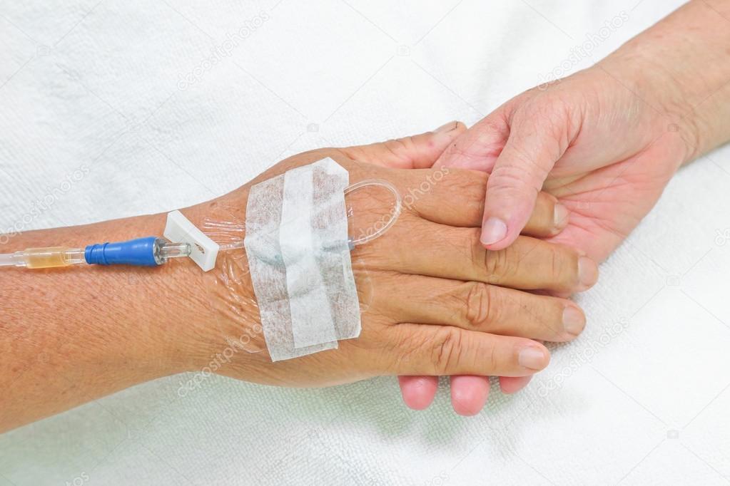 Old hands holding each other with IV solution in a patient's hand