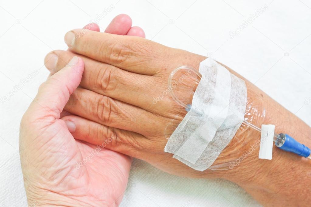 Old hands holding each other with IV solution in a patient's hand