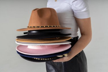 Gri arka planda poz veren bir sürü şapkası olan şık bir kadın. Moda, satış, alışveriş reklamcılığı. Anlaşıldı, metin için boşluk. Şapka seti kapanıyor. Eldeki şapkaların çeşitliliği.