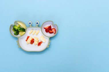 Sütten kesilme, blöf. İlk yeni yürümeye başlayan çocuk yemeği. Karışık sebzeli yumuşak eko plastik sofra takımı. Çocuk için sağlıklı beslenme, kendini besleme. Çocuk için kaşık parmaklı silikon tabakların üst görüntüsü.