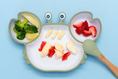 Sütten kesilme, blöf. İlk yeni yürümeye başlayan çocuk yemeği. Karışık sebzeli yumuşak eko plastik sofra takımı. Çocuk için sağlıklı beslenme, kendini besleme. Çocuk için kaşık parmaklı silikon tabakların üst görüntüsü.