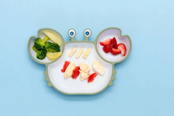 Childrens tableware.Soft eco plastic tableware with mixed vegetable. Healthy nutrition for kid, self feeding. Top view of silicone plate with spoon finger food for kid.