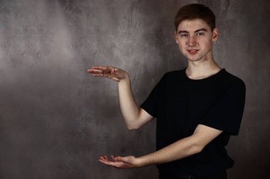 Genç adam gri arka planda metninizi ya da ürününüzü sunar ve gösterir