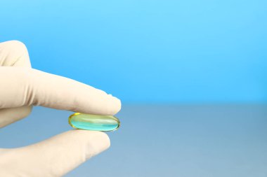 Doktor eldiven içinde bir Omega 3 kapsülü tutuyor.