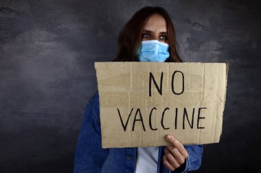 Üzerinde yazı olan bir kartonla tıbbi maskeli genç bir kadın. Aşı yok, aşı kavramını durdurun.
